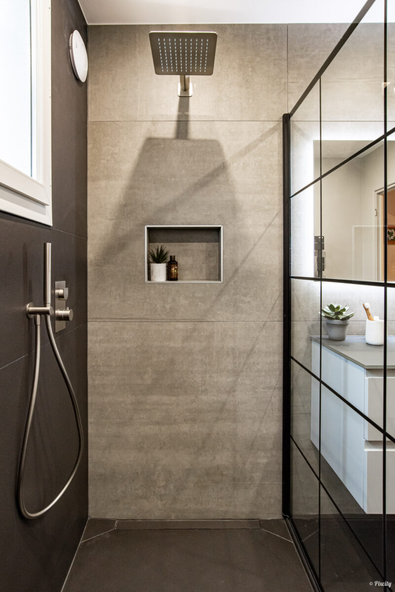 Idée déco salle de bain nature, détail douche italienne, carrelage grand format gris béton, niche encastrée avec plante succulente et flacon cosmétique, pommeau carré inox brossé, flexible douche inox, paroi verre transparent profilés noirs, miroir LED rétroéclairé, vanité blanche