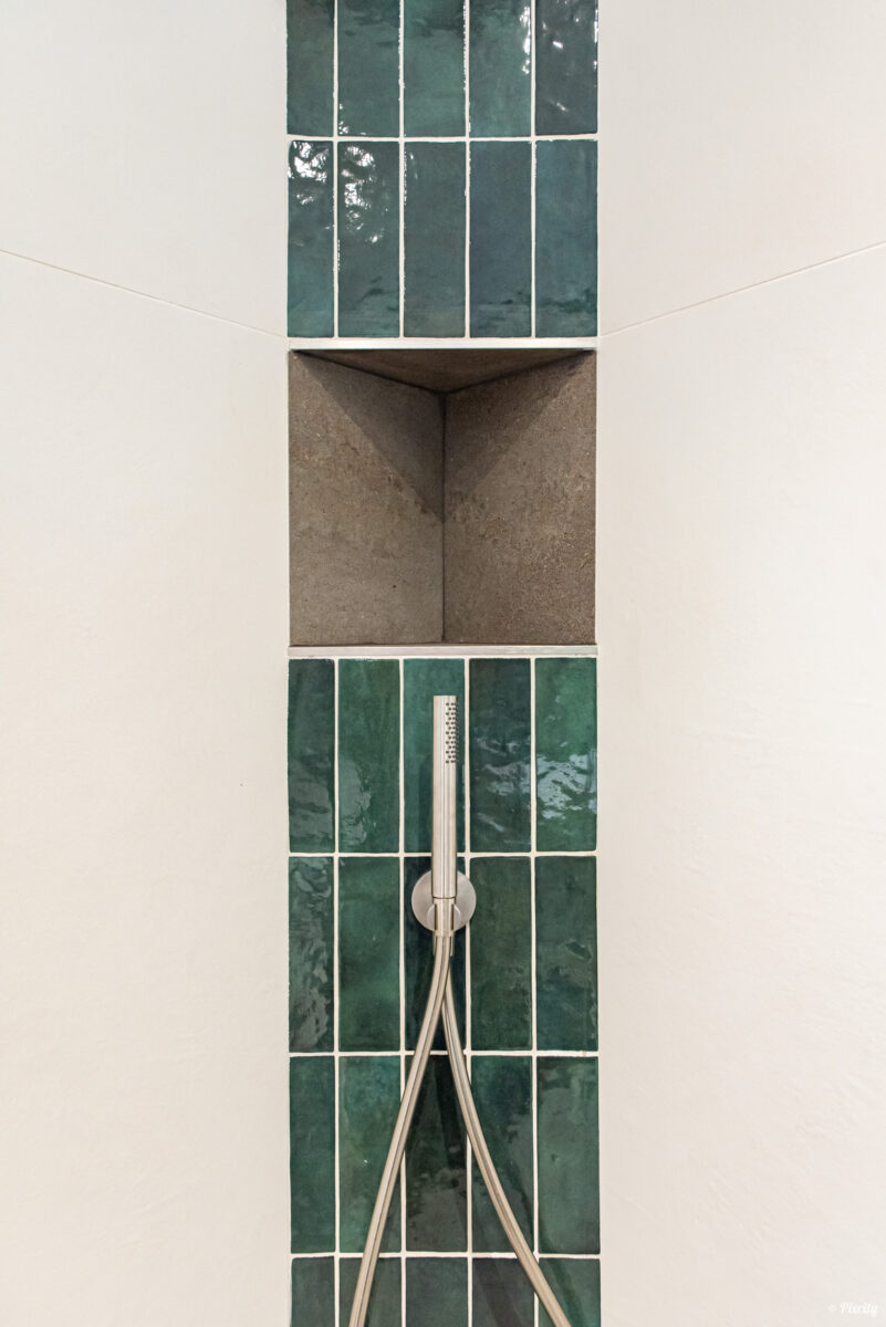 Idée déco salle de bain nature, détail douche italienne, carrelage zellige vert émeraude format rectangulaire vertical, niche encastrée béton ciré, douchette inox brossé flexible, paroi blanche lisse