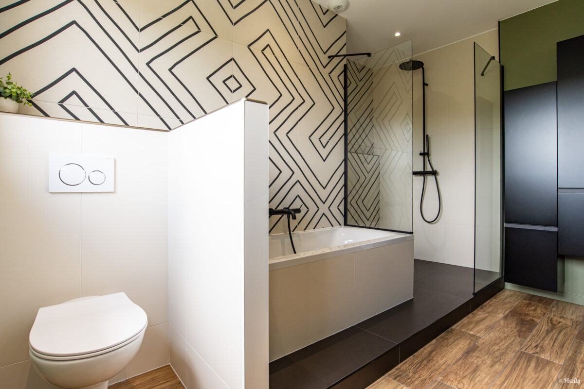 Idée déco salle de bain nature, WC suspendu blanc, carrelage géométrique graphique noir et blanc, douche italienne paroi verre droite, robinetterie noire mate, sol imitation parquet bois, cloison séparatrice WC blanche, mur vert olive