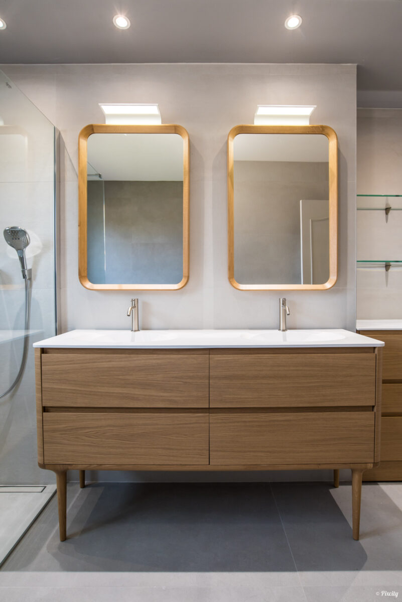 Idée déco salle de bain nature scandinave, détail double miroir rectangulaire cadre bois naturel éclairage LED, double vasque encastrée blanche, meuble chêne naturel sur pieds, robinetterie dorée inox brossé, étagères verre, carrelage mural blanc grand format