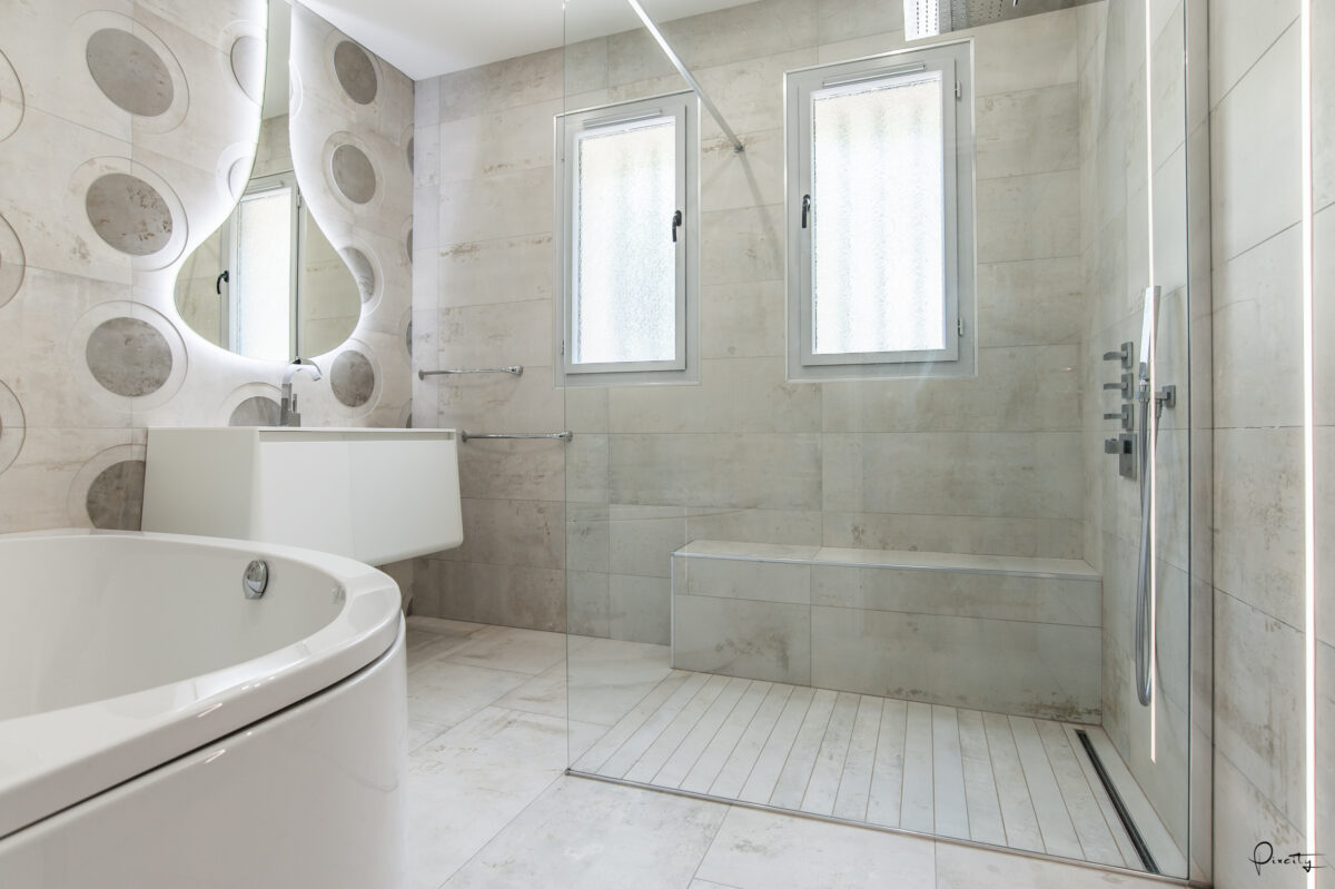 Idée déco salle de bain nature luxe blanc, baignoire ronde îlot blanche, miroir forme bulle lumineuse LED reflets ronds, vasque suspendue blanche, carrelage marbre gris veiné blanc grand format, douche italienne paroi verre, banc de douche marbre, fenêtres lumière naturelle