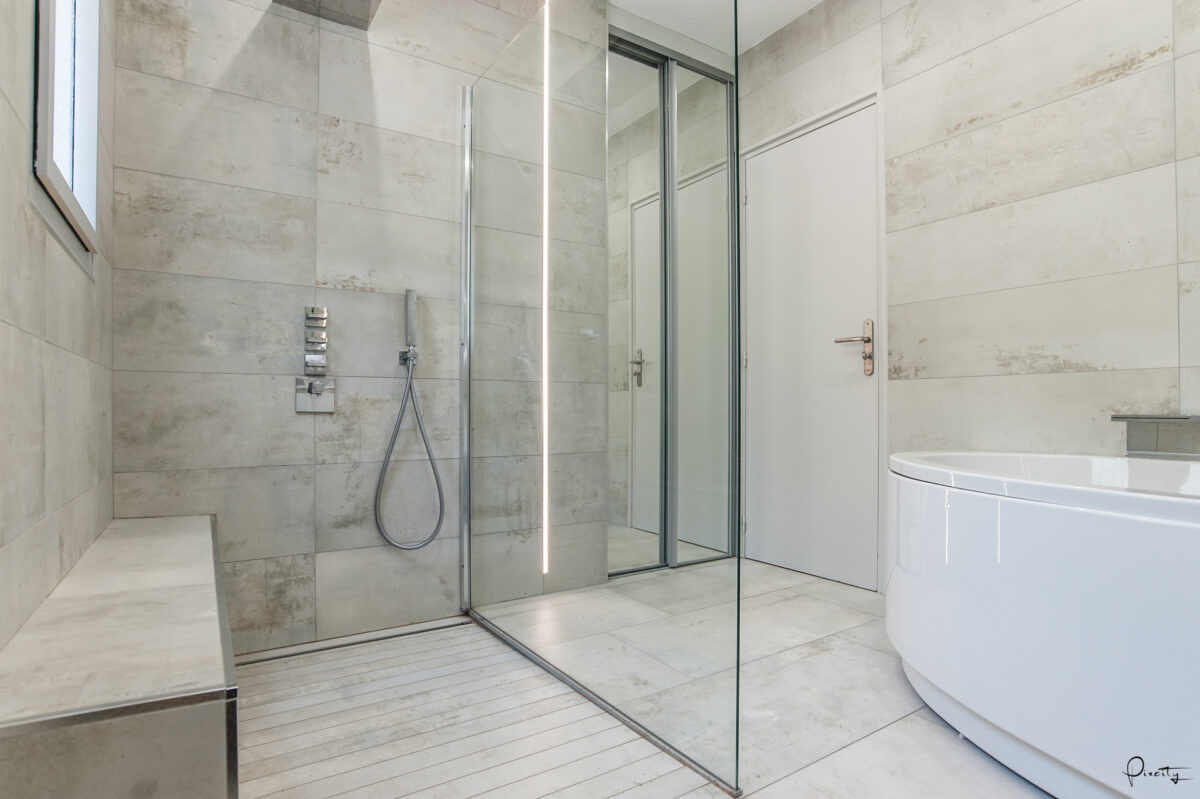 Idée déco salle de bain nature, douche italienne paroi verre miroir coulissant, banc de douche marbre encastré, robinetterie inox chromé, carrelage sol imitation bois lattes blanches, carrelage mural marbre gris clair veiné, baignoire angle blanche, porte bois naturel, lumière naturelle fenêtre