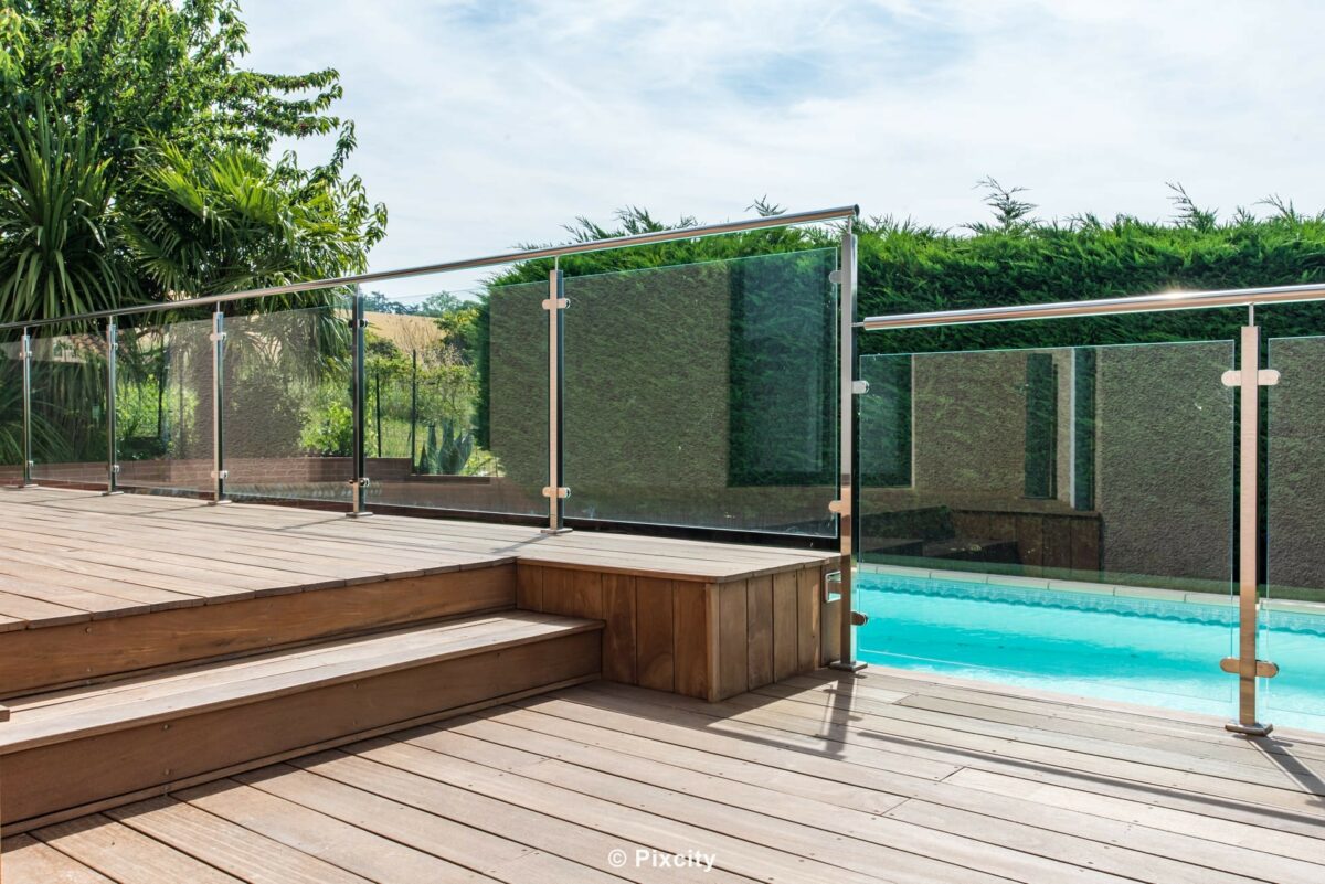 Aménagement terrasse bois autour piscine, terrasse bois exotique escalier deux niveaux garde-corps verre inox poli, piscine rectangulaire bleue en fond, maison contemporaine, palmier yucca, végétation jardin méditerranéen